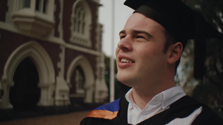 Graduating senior wearing graduate wear outdoors on the campus smiles and talks