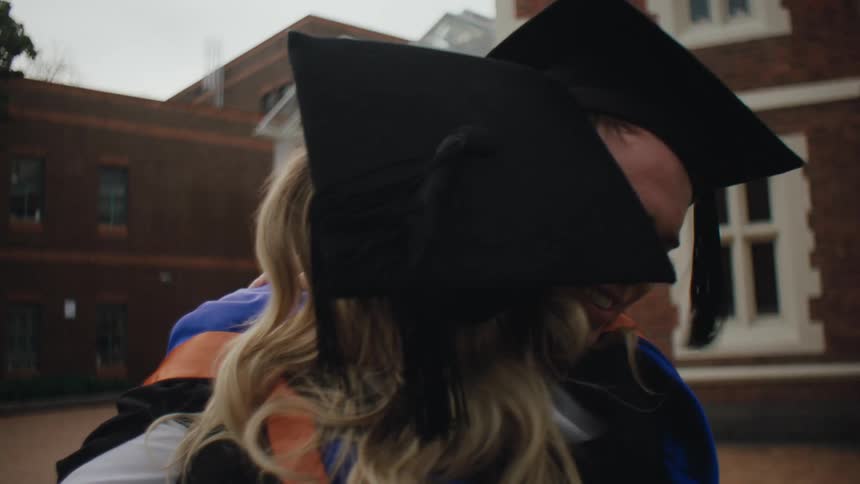 Man and woman hugging while both wearing graduation robes