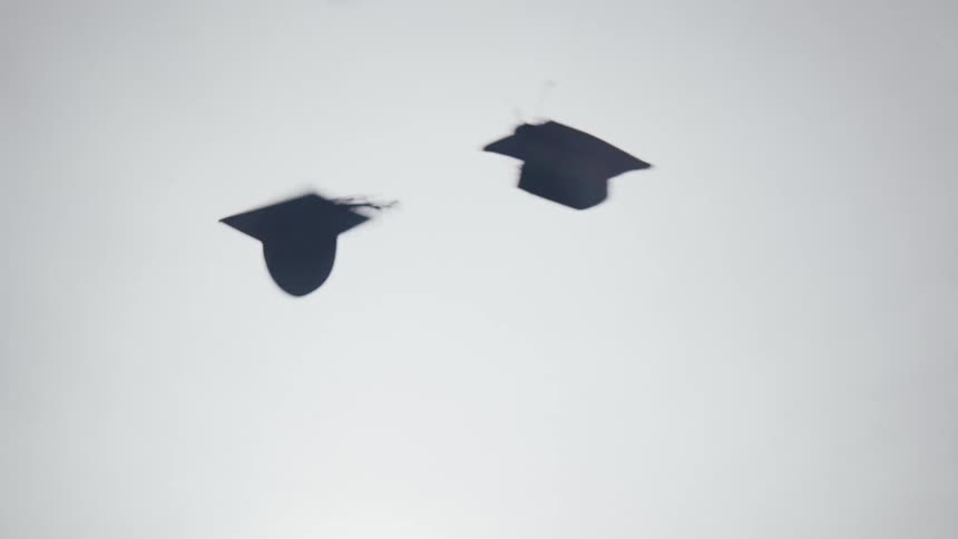 Group of students in graduation gowns throwing their graduation hats into the air