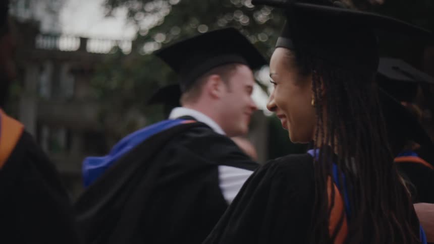A group of people in graduation gowns and caps celebrate by hugging each other
