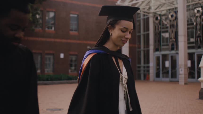 Man and woman with graduation gown walking together