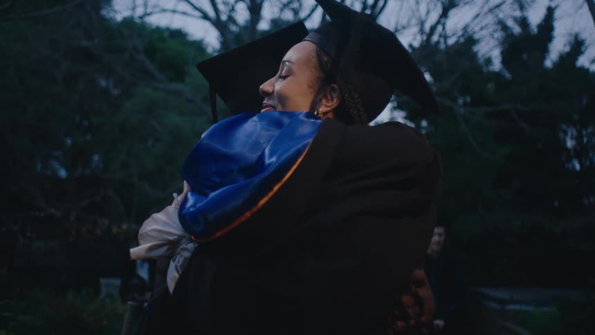Two young students hugging each other while wearing graduation robes