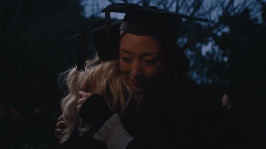 Two friends hugging each other wearing graduation gowns