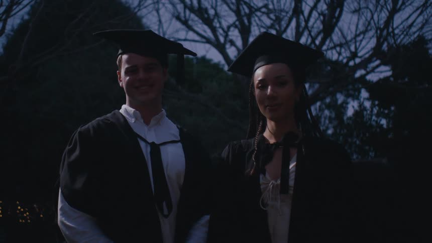 Woman and man standing side by side smiling and both wearing graduation gowns