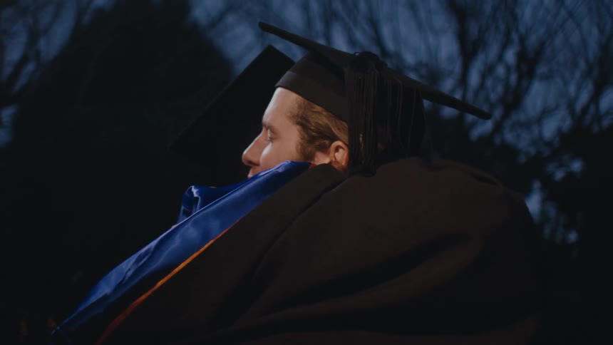People in graduation gowns and caps celebrate by hugging each other at night
