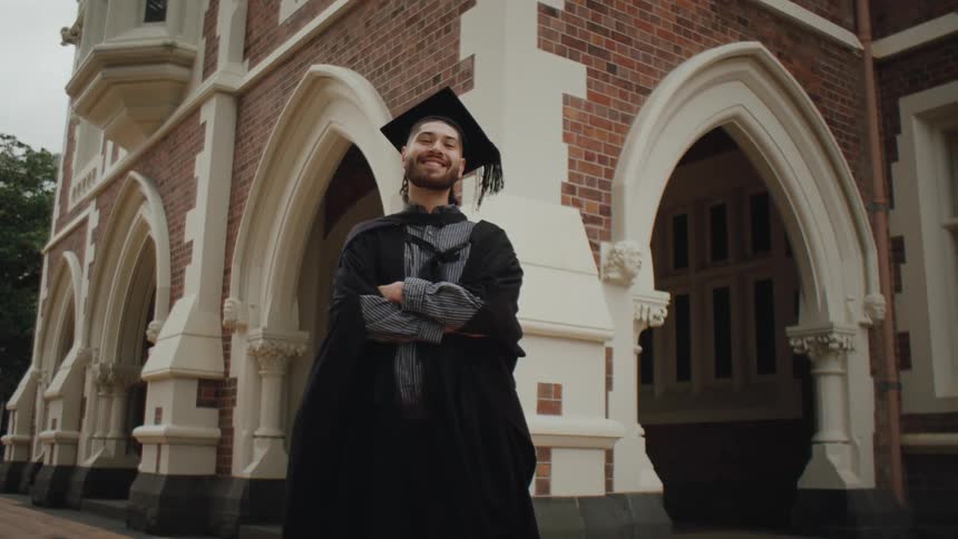 Happy man with arms crossed posing wearing graduation gown