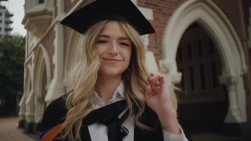 Woman fingers her hair as she smiles in her graduation outfit