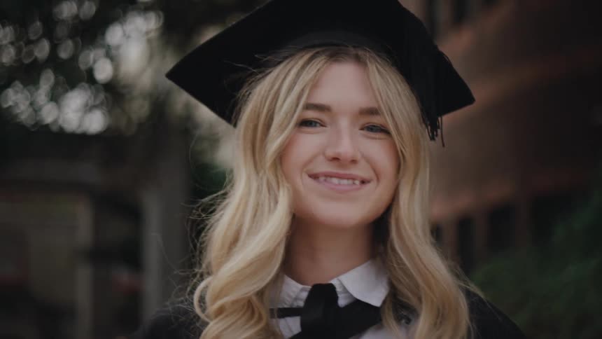 A young woman with long wavy blonde hair wearing a black academic cap and gown