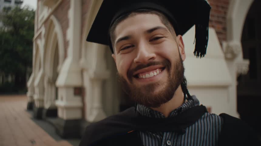 Male graduate wearing a cap and gown smiling for the camera outdoors