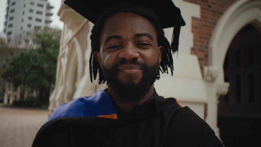 Man in graduation regalia smiles with pride