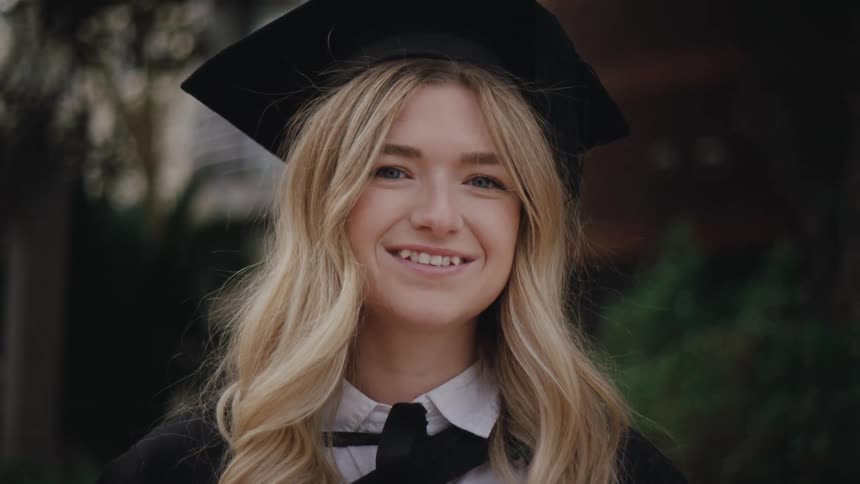 A young blonde woman in a black and white graduation outfit smiles at the camera