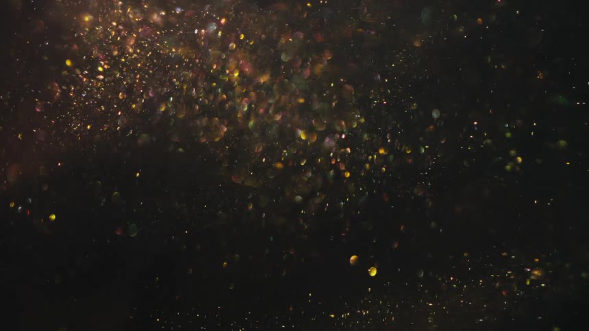 Swirling patterns of gold scattered glitter floating against a dark background