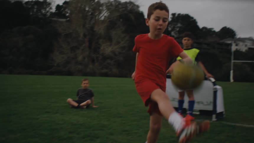 A small child on a red shirt playing soccer on a grassy field