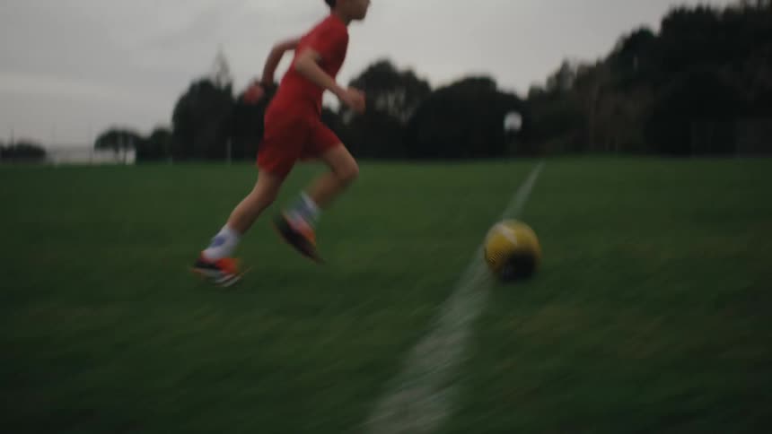 A boy in a red uniform runs across a green field during soccer practice