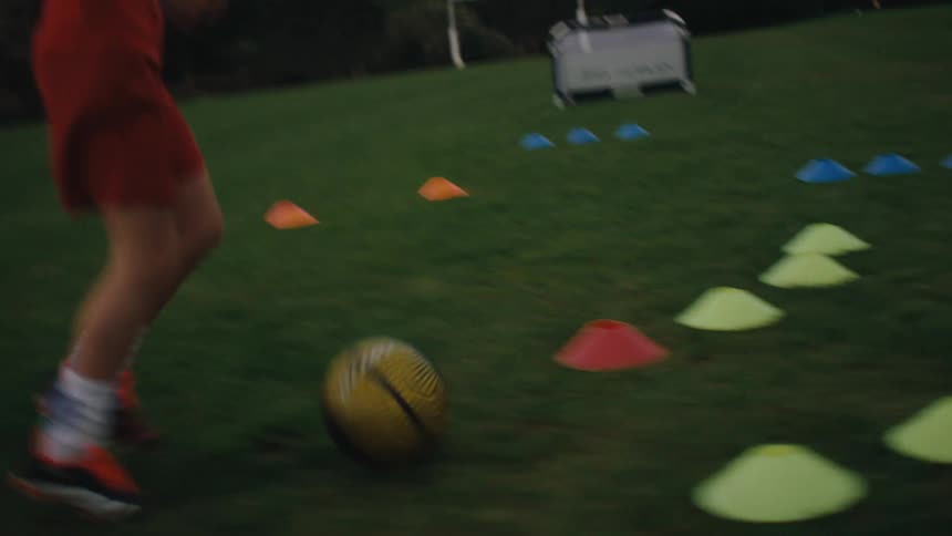 Boy dribbling around cones on grass