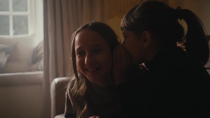 A teenage girl laughs when another girl whispers in her ear