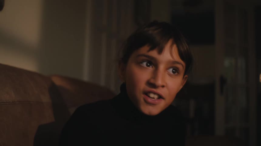 A girl in a black sweater sits on a brown couch having a conversation