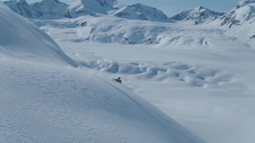 Person rides a snowmobile down a steep snow covered slope in the mountains on a winter day