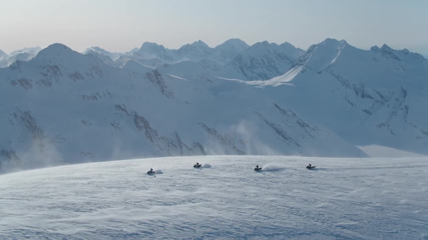 Four people on snowmobiles traveling through snowy mountains