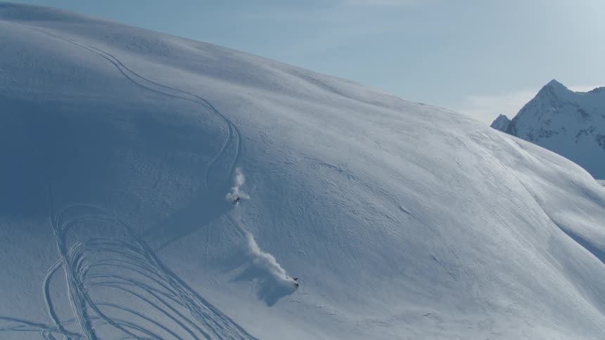 A snowmobile descends a steep snowy slope with rugged mountains in the background