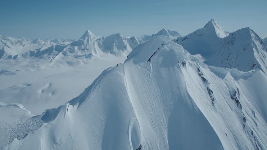 A vast expanse of snowcapped mountains stretches across the horizon under a clear blue sky