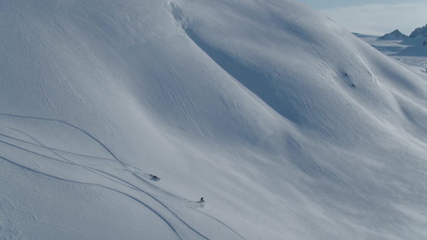 Two people each with a snowmobile going down a mountain