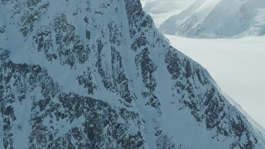 A lone skier is making their way down the steep snow covered slope leaving faint tracks on the mountainside