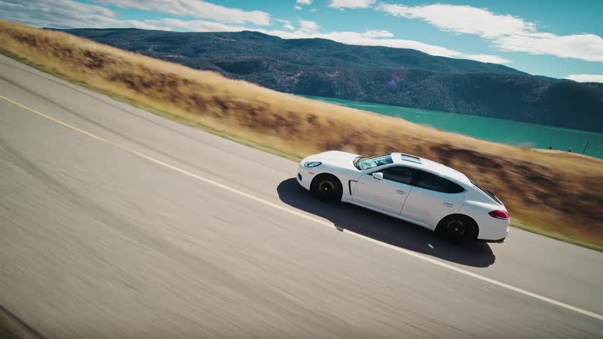 White sports car driving on a road next to a body of water and mountains
