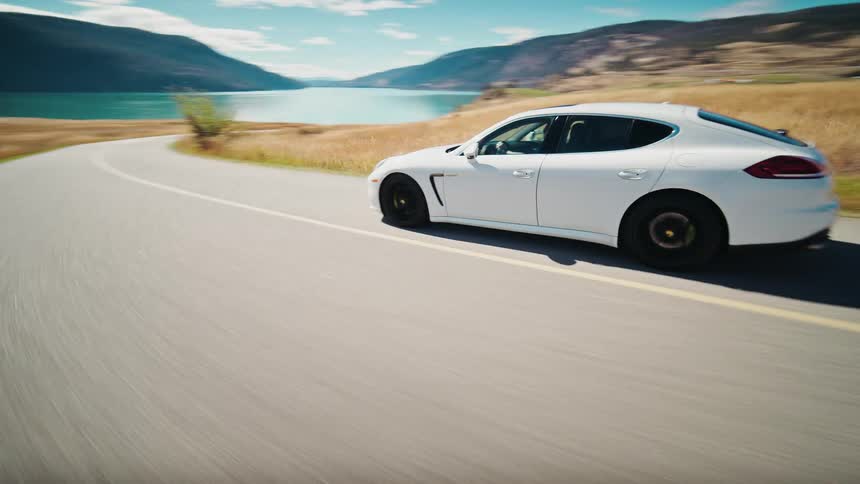 Aerial view of a white sports coupe car traveling along a lakeside road