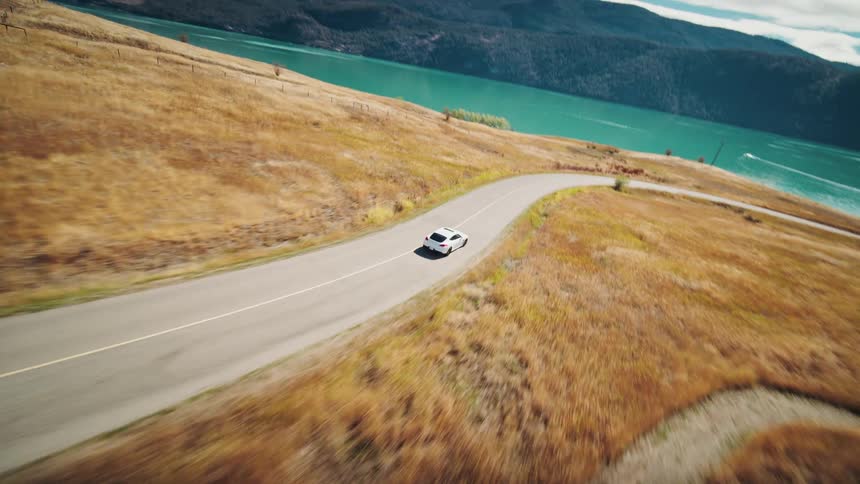 Aerial view of a white sports car traveling through a valley and along a lakeshore