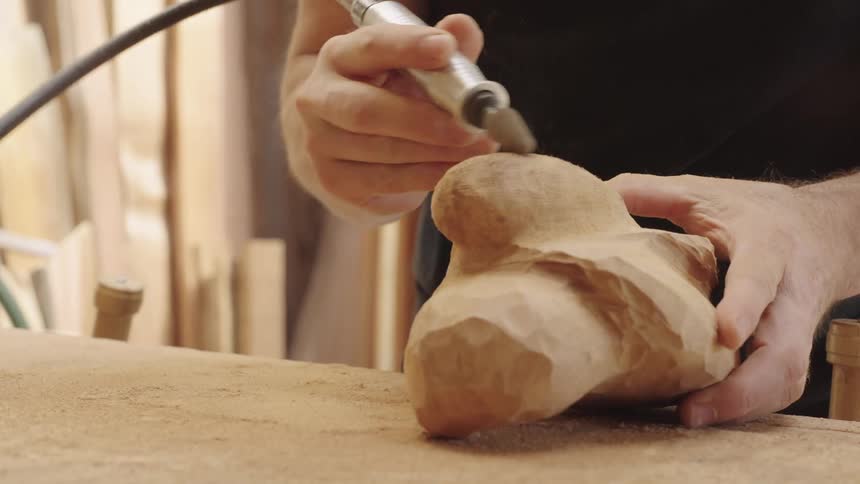 A person uses a rotary tool to shape a piece of wood