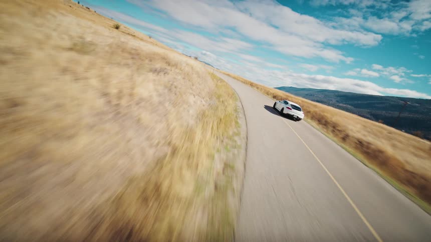 Aerial view of a white sports car traveling along a lakeside road