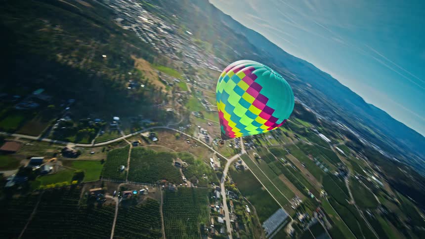 A colorful hot air balloon floats over a rural landscape with rolling hills and farmland