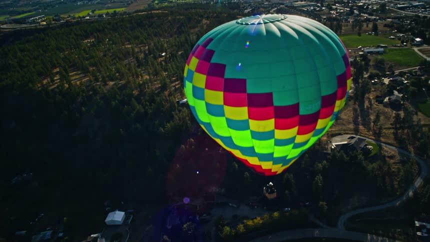 A colorful hot air balloon floats over a rural landscape with rolling hills and farmland
