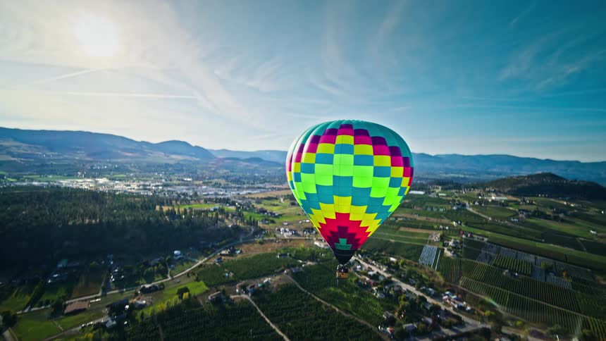 Colorful hot air balloon flying over a landscape with green fields trees and a city in the background