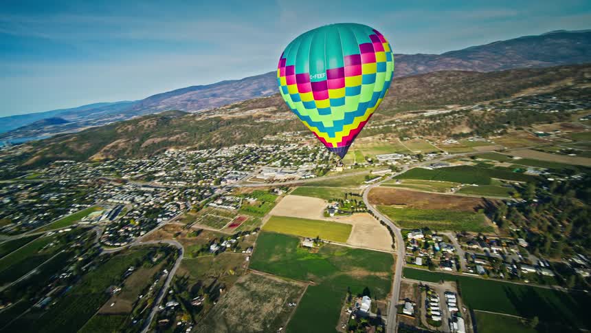Aerial panorama of a colorful balloon flying over an urban city and mountains