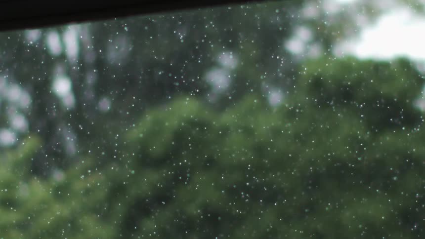 Raindrops falling on a window with a blurred background of greenery