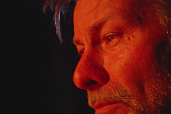 Closeup of a mans face his sad eyes reflecting the glow of a nighttime campfire