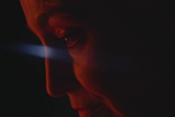 A close up of the face of a nervous woman under red lights at night