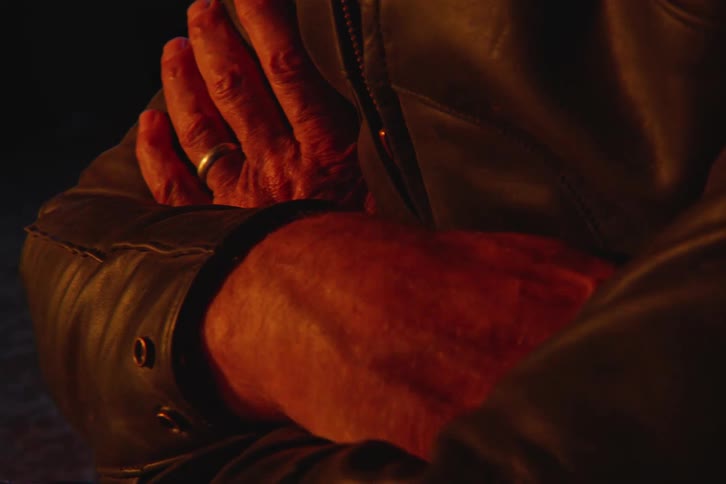 Man in leather jacket with arms crossed sitting outdoors at night