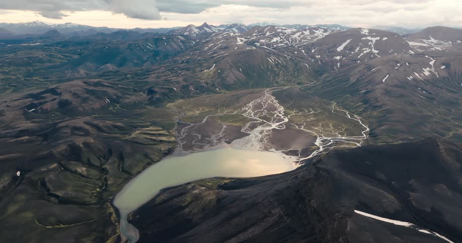 Aerial view of a mountainous landscape with a large body of water surrounded by intricate patterns of channels and varied terrain textures