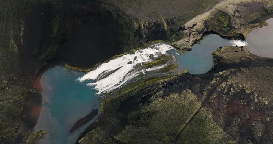 Aerial view of a river cascading down a green mountain