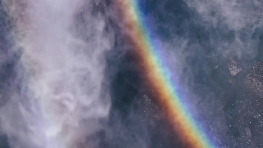 A vibrant rainbow cuts through mist over a body of water