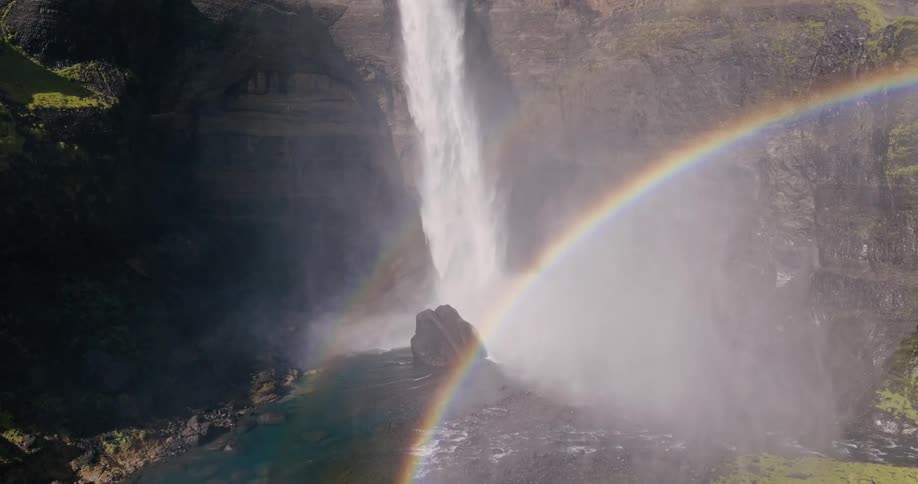 Aerial of a rapidly cascading waterfall forming a double rainbow in the canyon