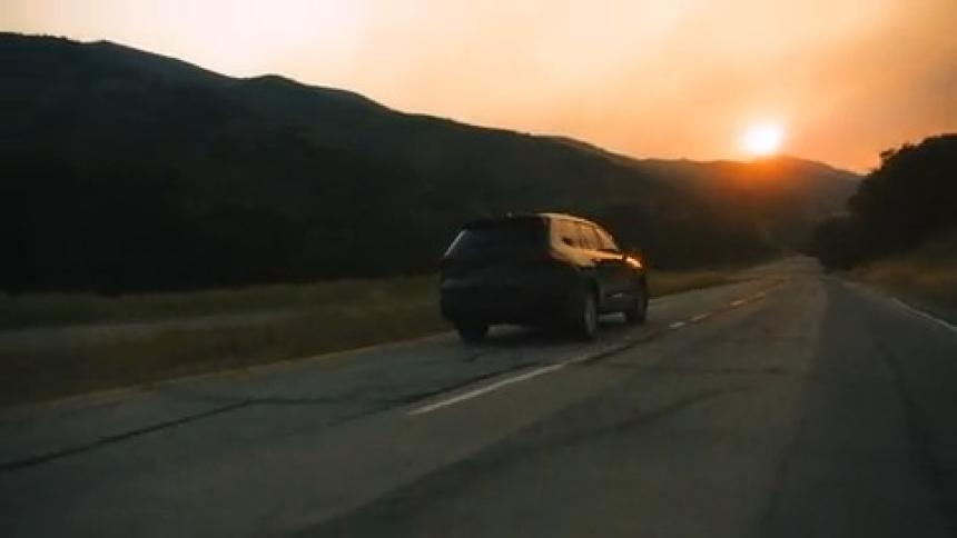 Car driving on a road towards the sunset with hills in the background and a golden sky