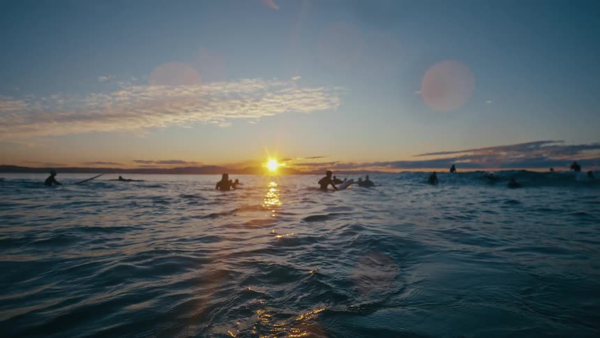 Silhouette of people surfing in the ocean on a morning with the sun on the horizon