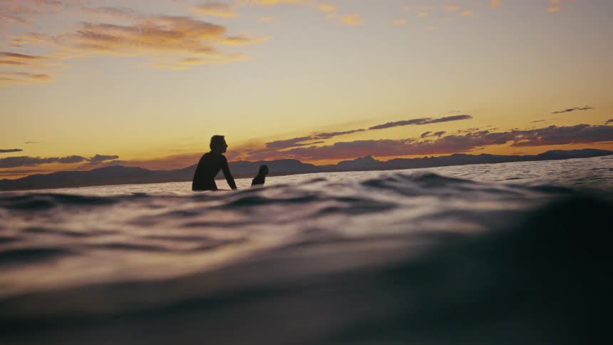 Silhouette of a surfer floating over a surfboard in a calm ocean at sunset