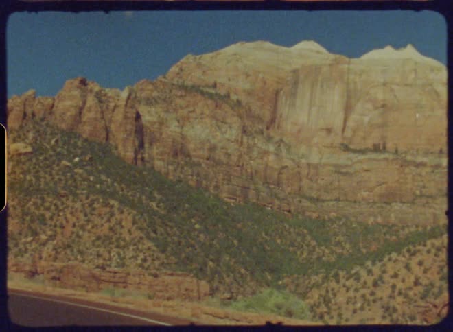 Two cars drive along a curved road through a canyon with tall walls captured on vintage film