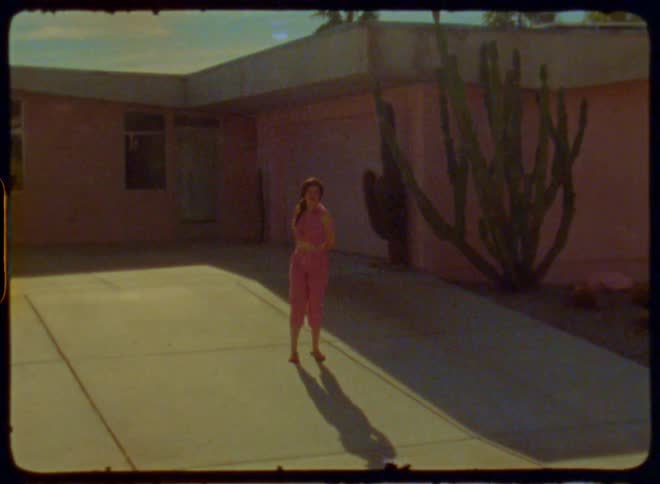 A woman on wearing pink vintage clothes stands in front of a pink house