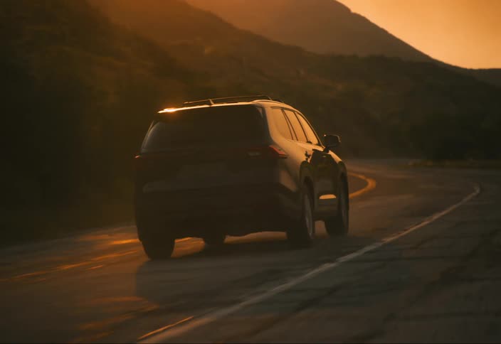 A black suv drives down a highway at sunset